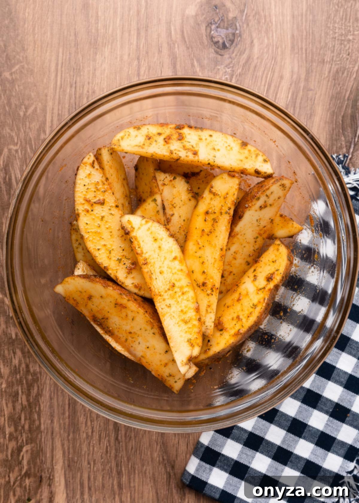 wedged russet potatoes in a glass bowl coated with olive oil and ground spices