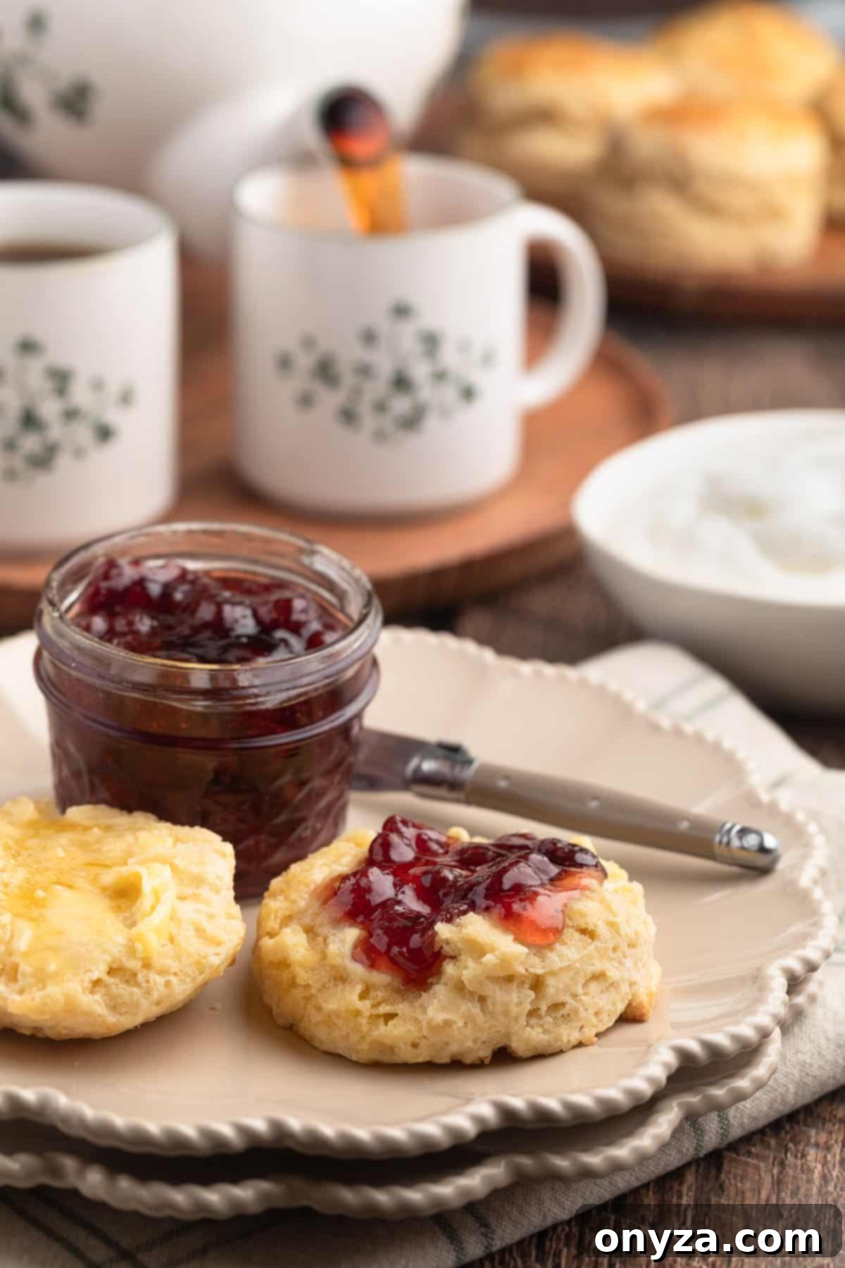 Irish scone on an ivory plate spread with butter and jam with a cup of tea being poured in the background