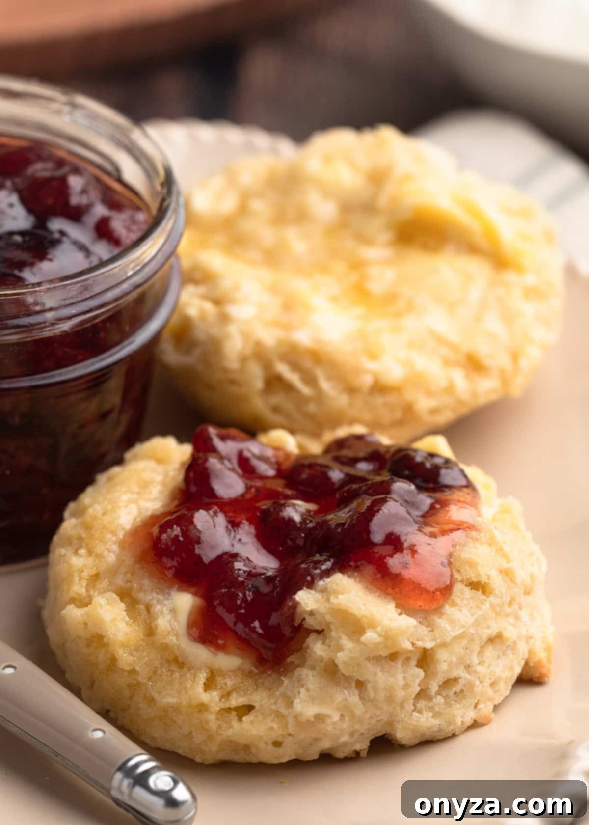 closeup of two halves of an Irish scone on an ivory plate. One half is spread with butter and jam and the other is just spread with butter.