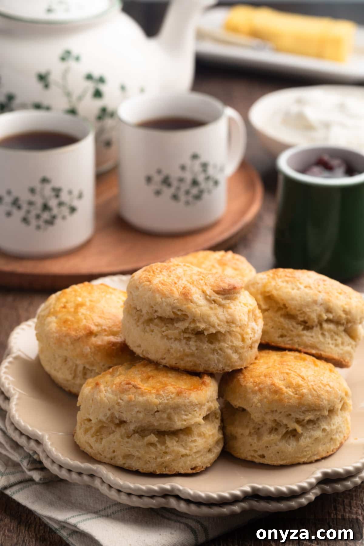 Irish Scones on an ivory plate, with a tea set in the background and bowls of whipped cream and jam