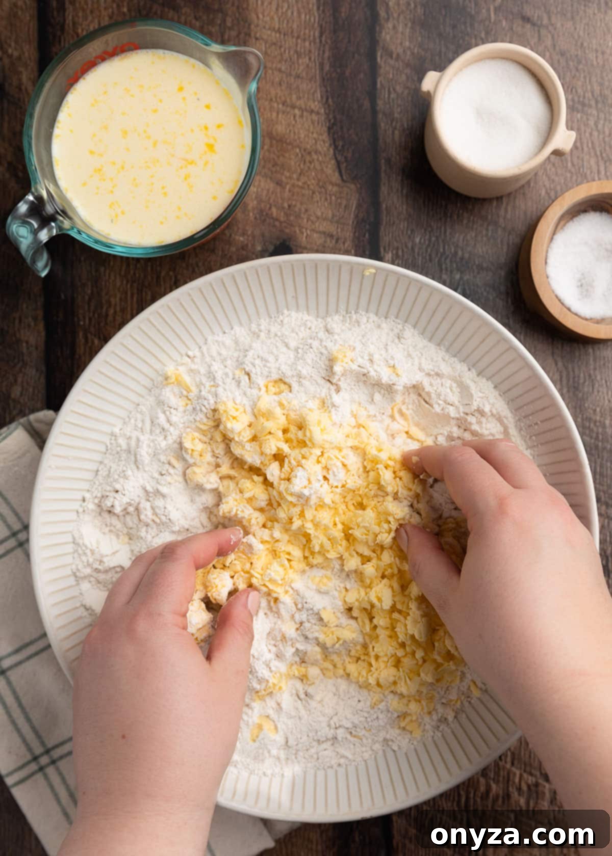 overhead photo of grated butter being incorporated into a bowl of dry ingredients by hand