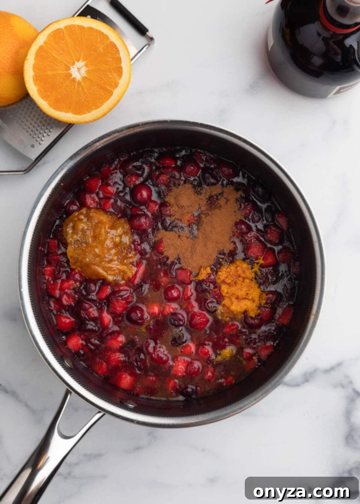 Orchard Citrus Cranberry Sauce 7 An overhead shot of simmered apple cranberry sauce in a saucepan, with fresh orange marmalade, orange juice, orange zest, and ground spices artfully arranged around it, ready to be incorporated.