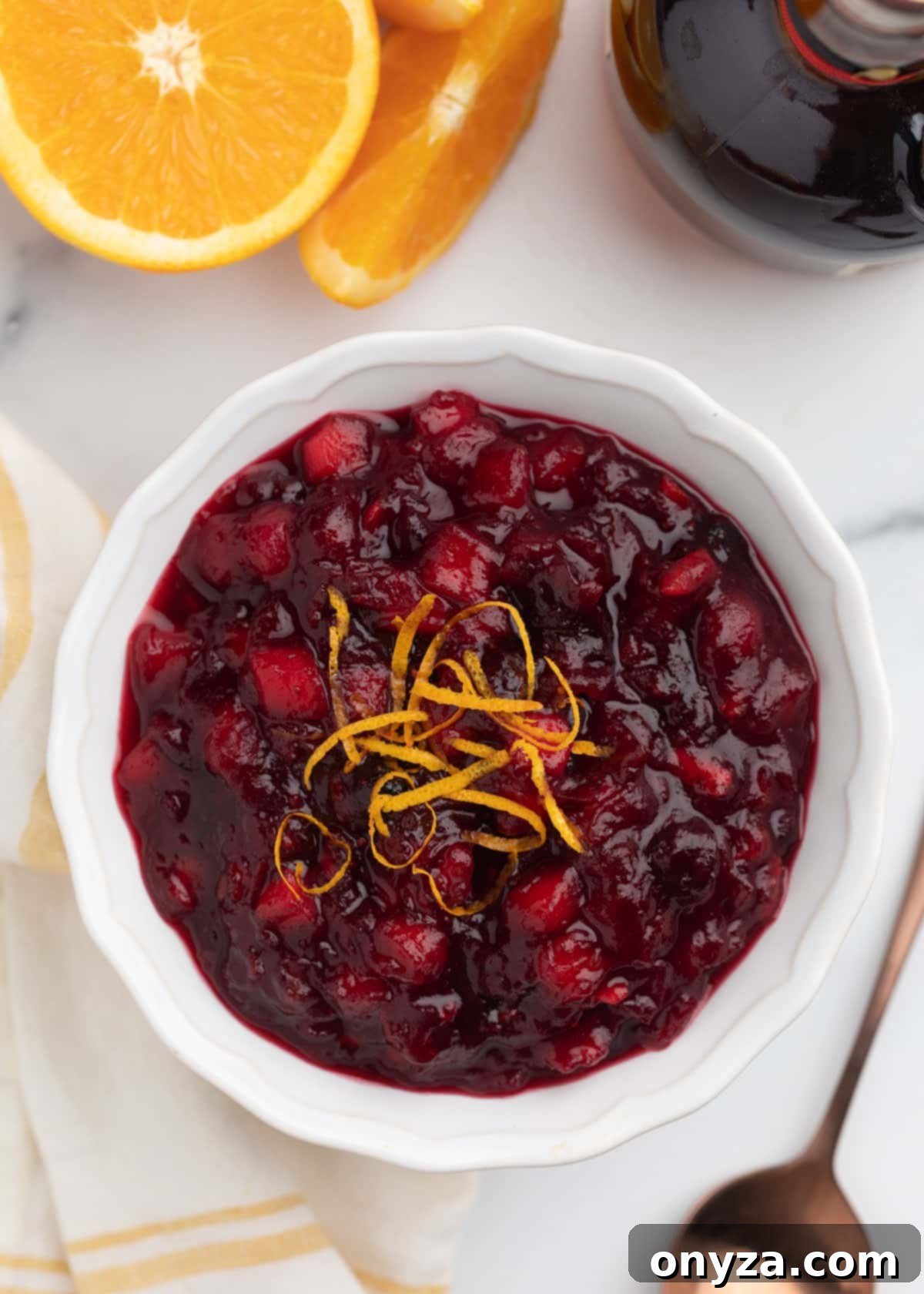 Orchard Citrus Cranberry Sauce 10 An inviting overhead shot of luscious apple orange cranberry sauce, artfully presented in a pristine white bowl and elegantly garnished with delicate spirals of fresh orange zest. This highlights its vibrant color and appealing texture.