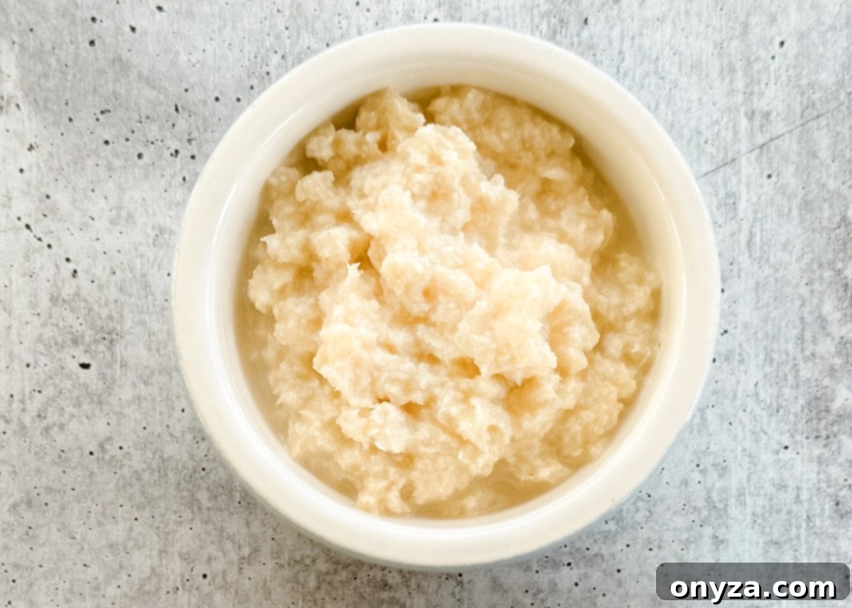 The Fiery Root 4 An overhead shot of prepared horseradish, a finely grated, bright white condiment, served in a small bowl on a textured gray board.