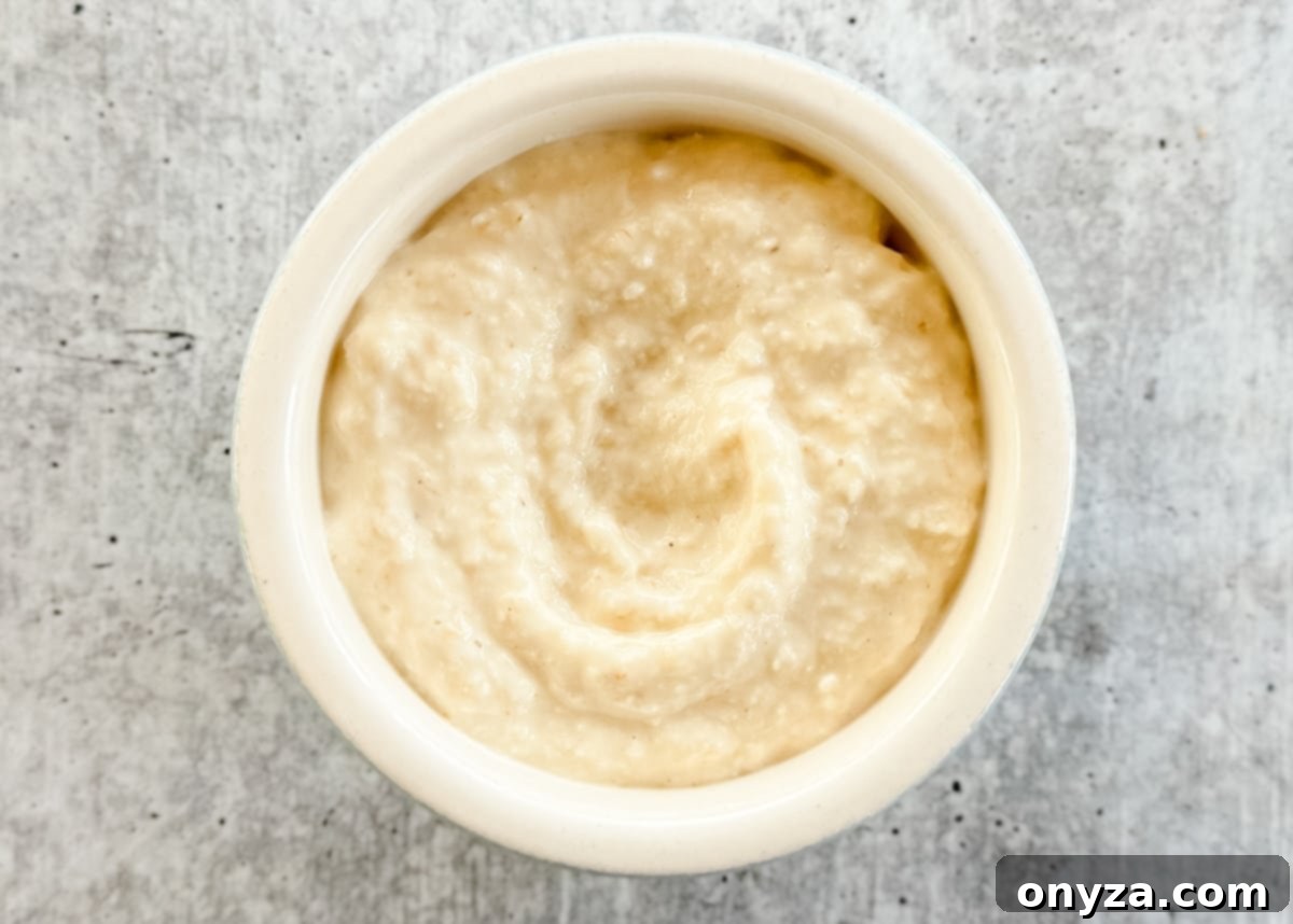 The Fiery Root 5 An overhead shot of cream-style horseradish, a smooth, off-white sauce, presented in a small bowl on a textured gray board.