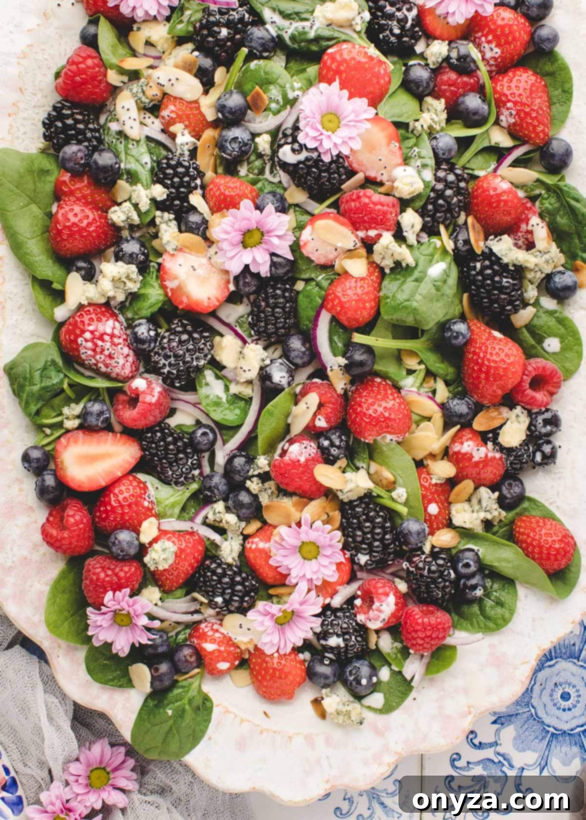 Vibrant spinach berry salad elegantly arranged on an ivory oval platter, beautifully garnished with delicate pink edible flowers.