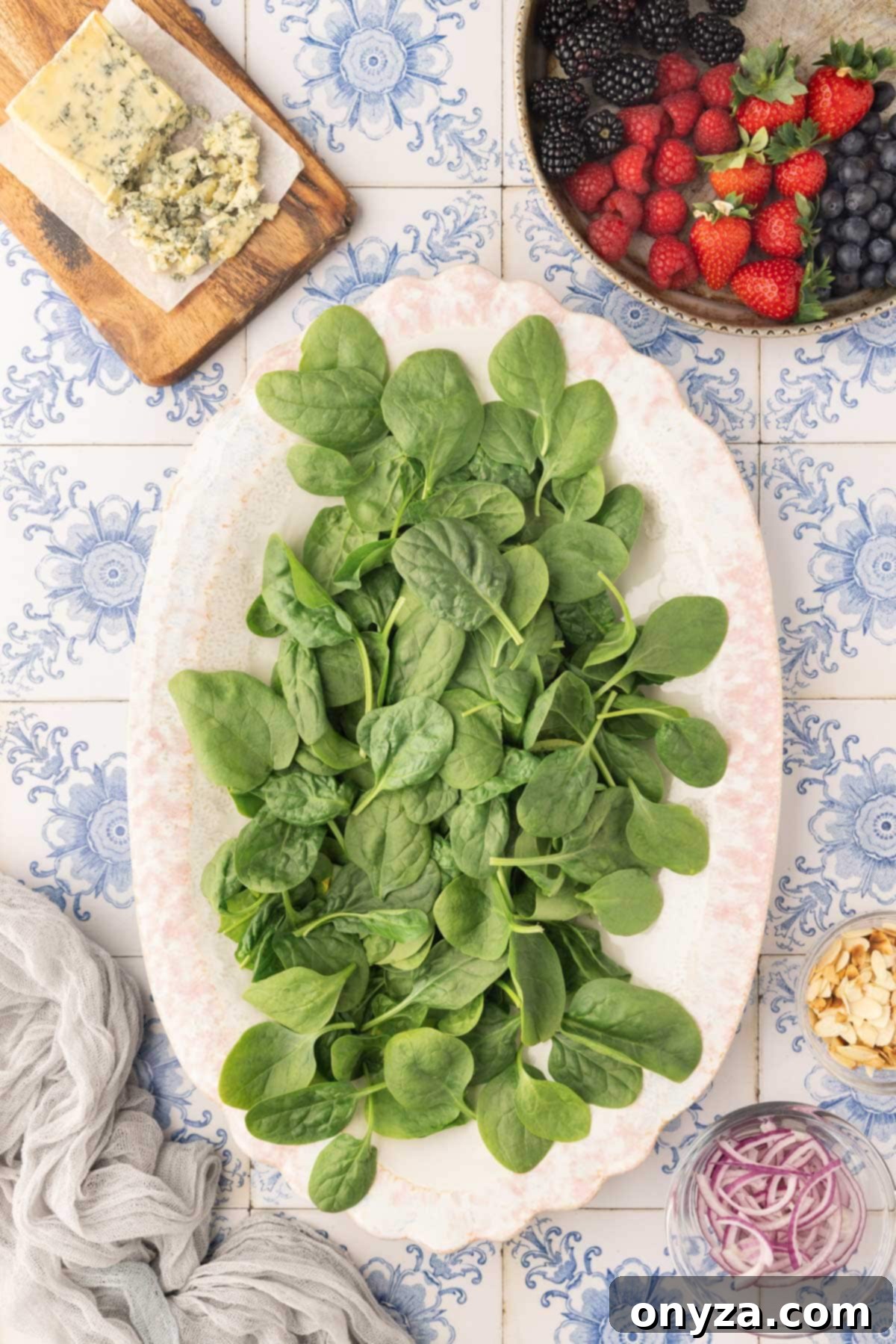 Overhead view of fresh baby spinach leaves gracefully spread on an oval ivory platter, set against a charming blue tile background.
