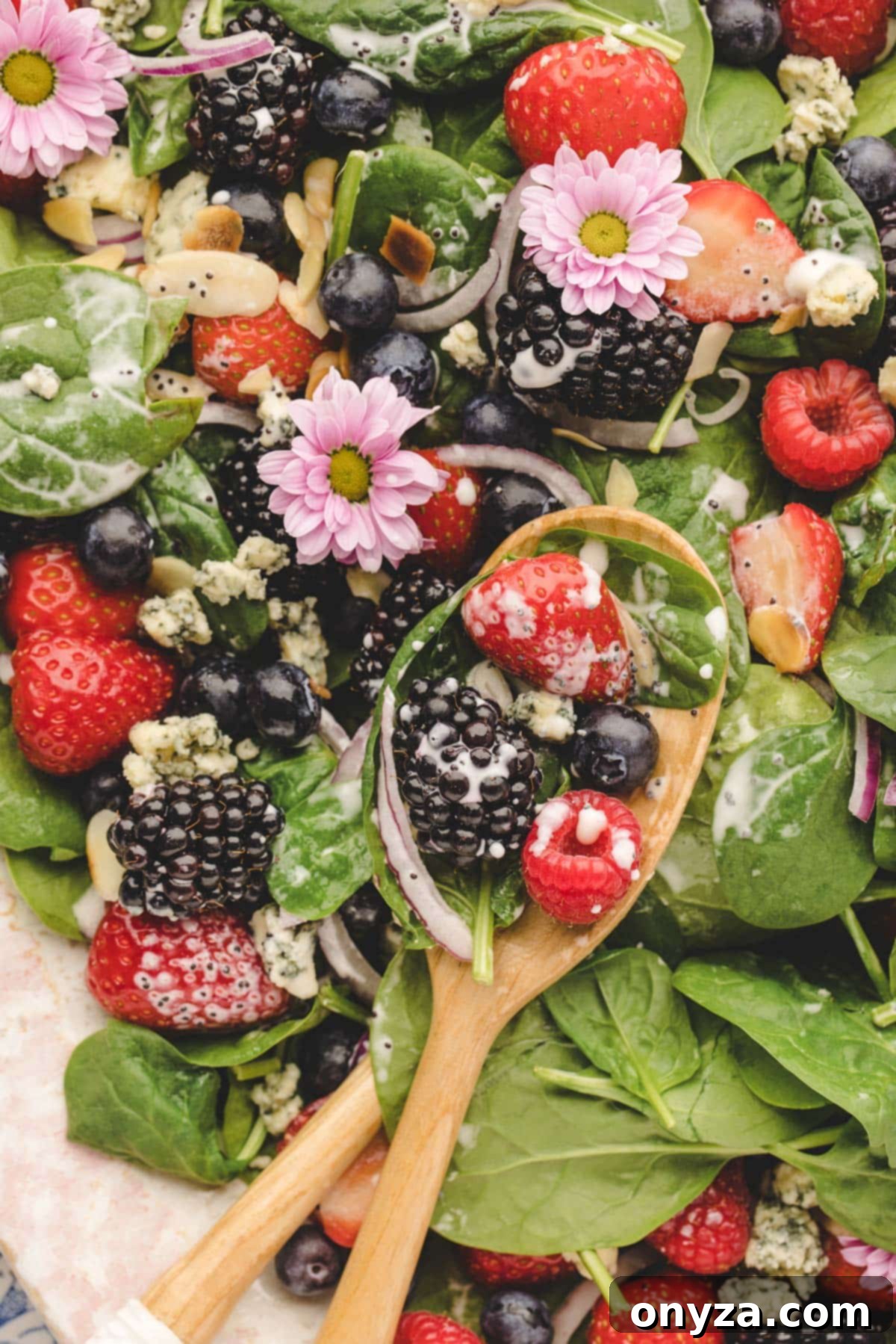 A close-up view of a perfectly dressed spinach berry salad on a platter, accompanied by elegant salad spoons, ready for serving.