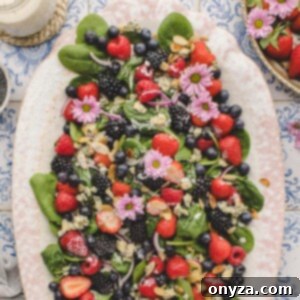 overhead of spinach berry salad on an ivory oval platter, garnished with pink edible flowers