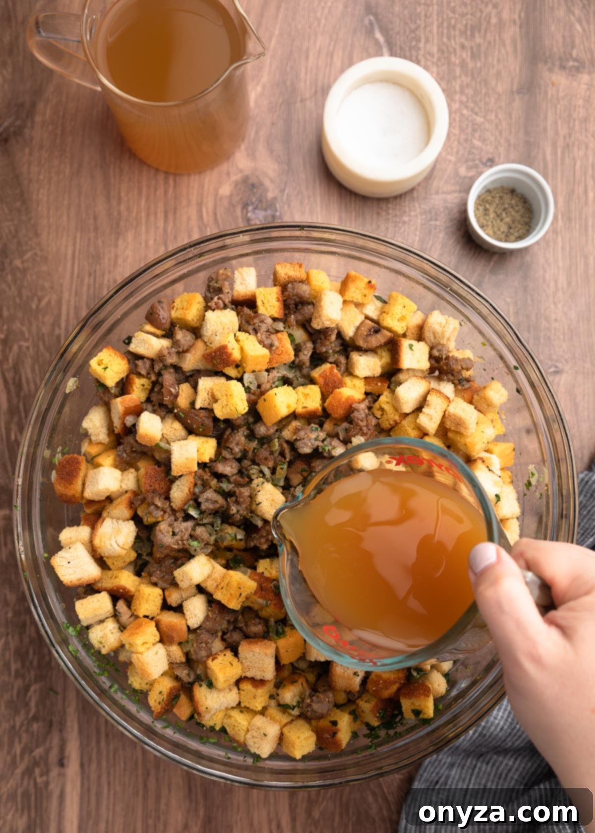 Festive Sausage and Chestnut Stuffing 13 pouring apple cider and stock from a liquid measuring cup into a bowl of croutons, sausage, and seasonings.