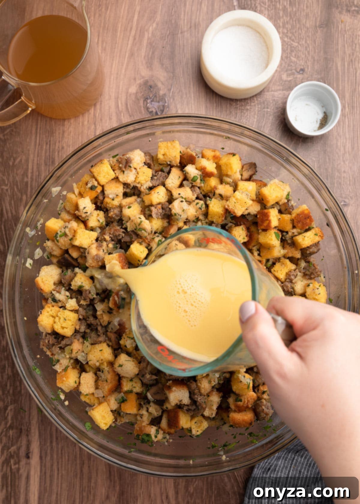 Festive Sausage and Chestnut Stuffing 14 pouring beaten eggs and stock from a liquid measuring cup into a bowl of croutons, sausage, and seasonings.
