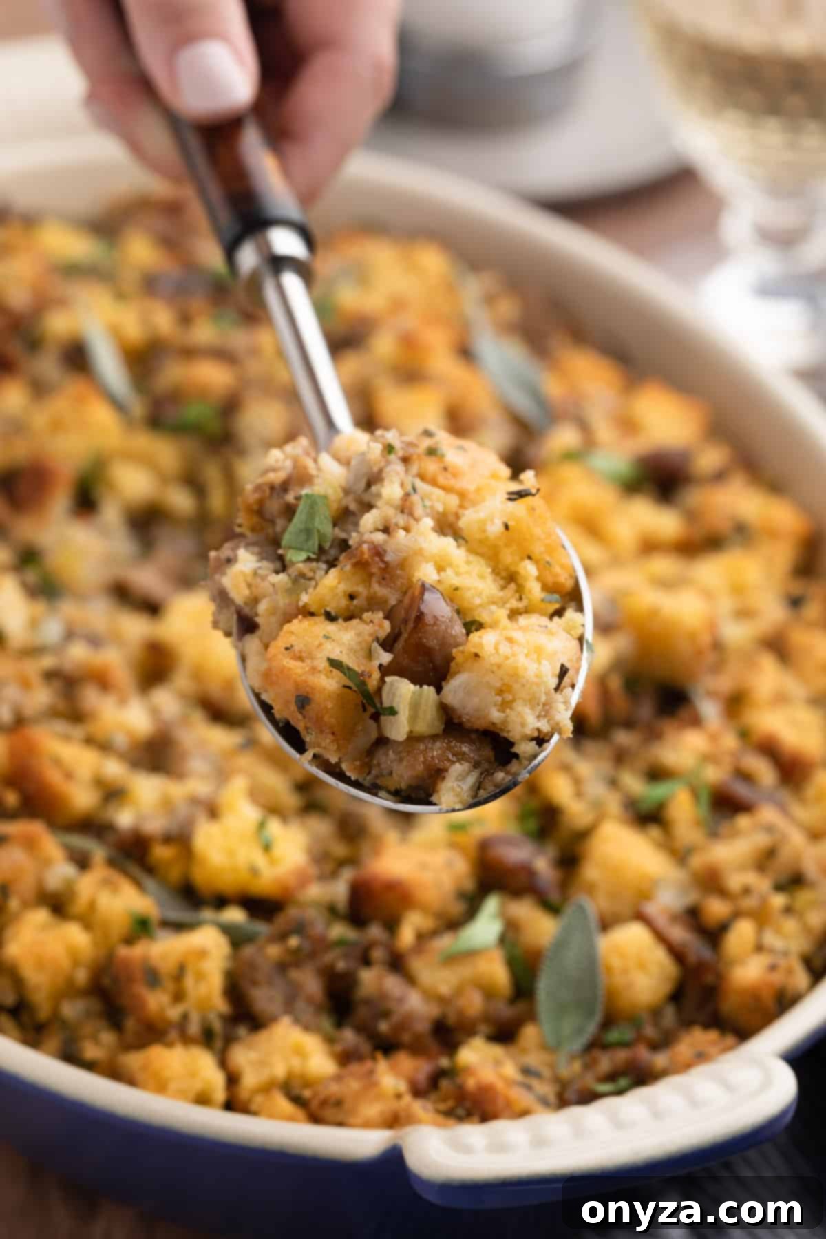 Festive Sausage and Chestnut Stuffing 17 a scoop of sausage and chestnut stuffing being held over a gratin pan of baked stuffing with a serving spoon