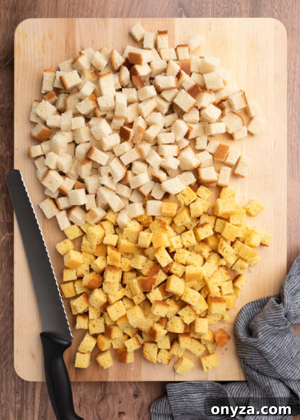 Festive Sausage and Chestnut Stuffing 4 overhead of country white and cornbread cubes on a wooden cutting board with a bread knife