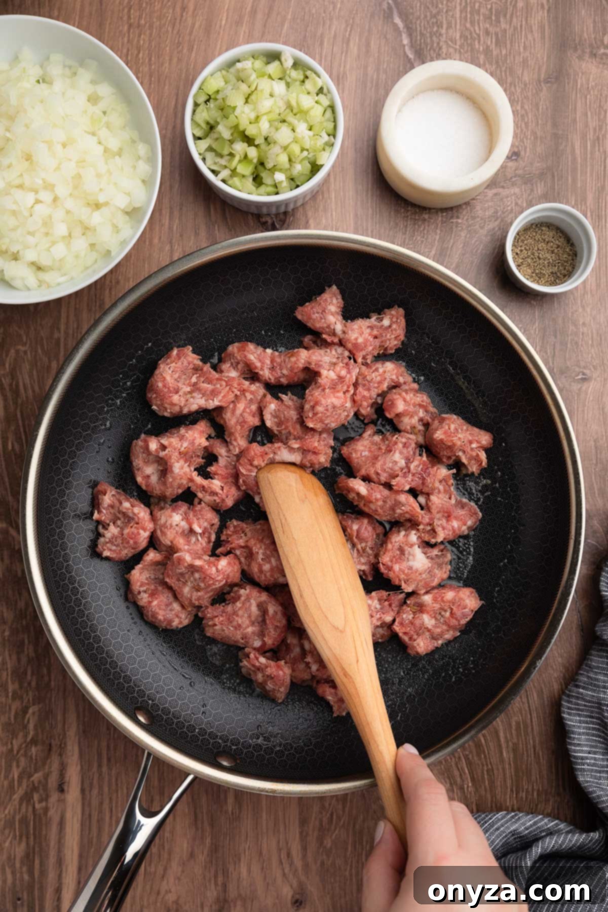 Festive Sausage and Chestnut Stuffing 7 raw Italian sausage meat being stirred in a skillet with a wooden spoon