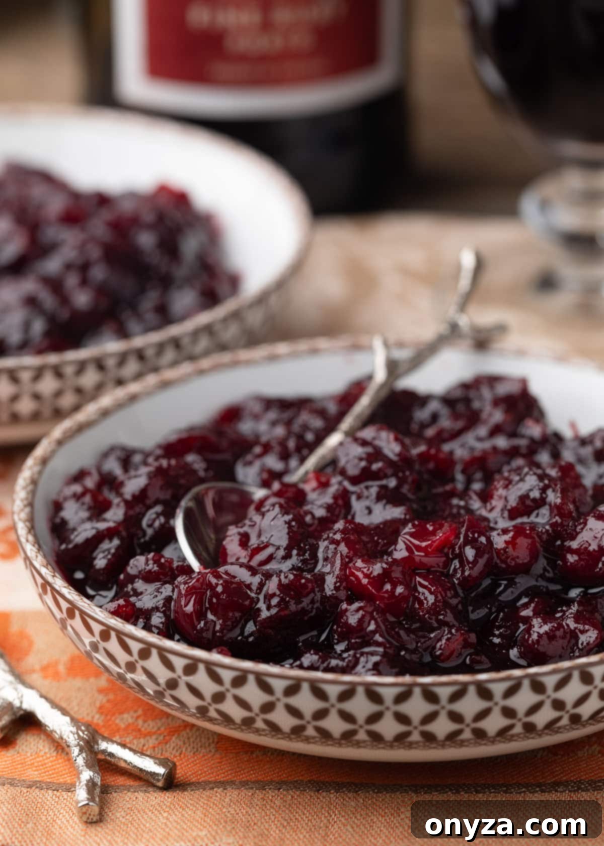 port cranberry sauce in a brown and white patterned bowl with a silver branch motif spoon on an orange damask napkin