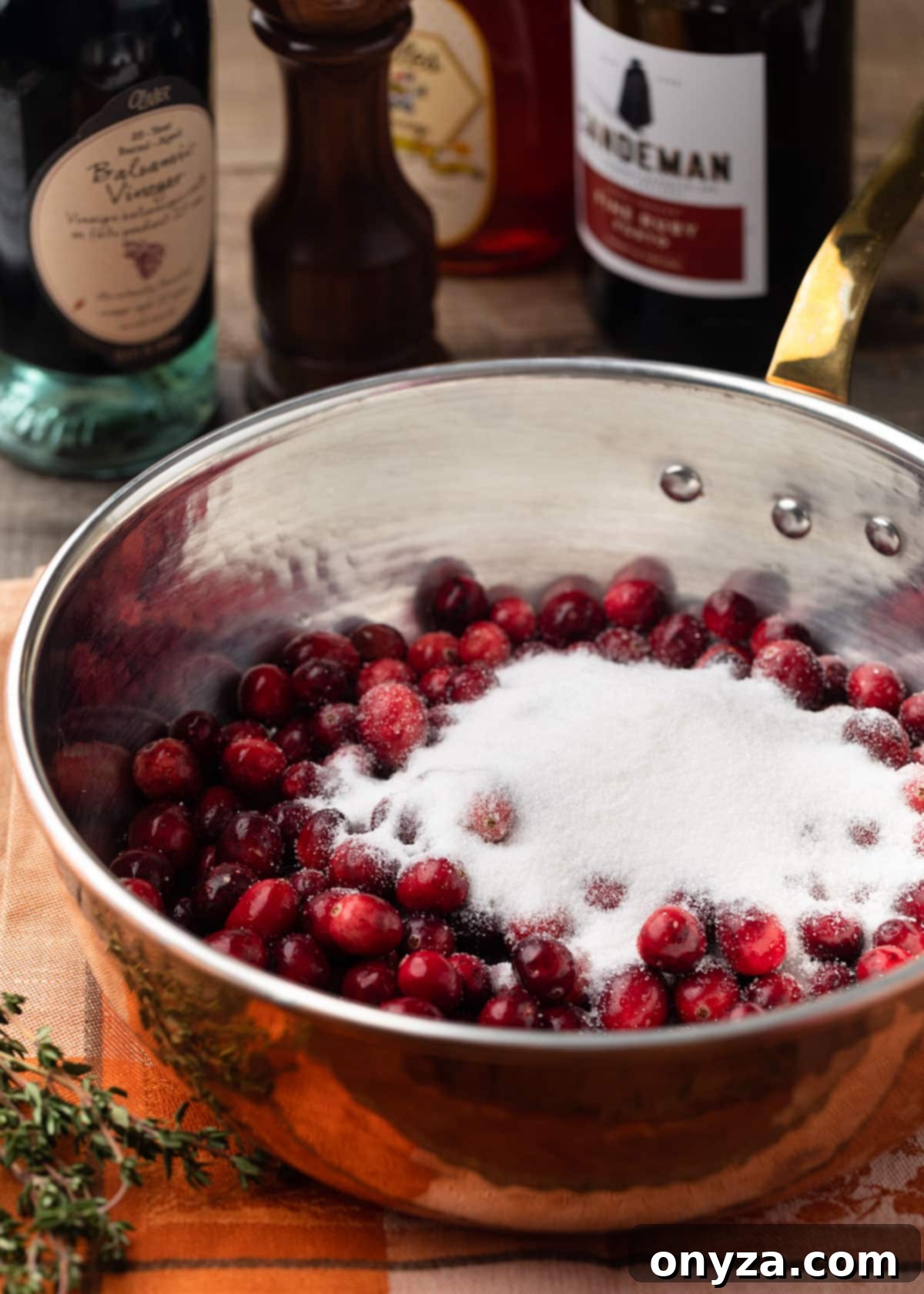 copper saucepan filled with whole fresh cranberries and granulated sugar on an orange napkin