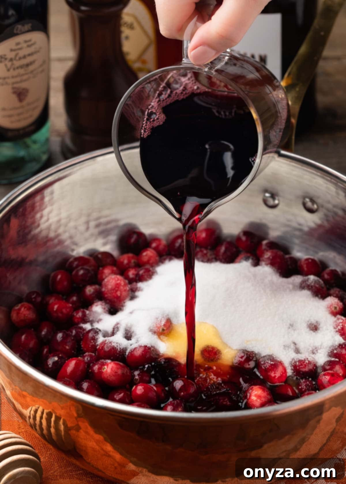 pouring a mixture of port wine and water into a copper saucepan filled with fresh cranberries and granulated sugar