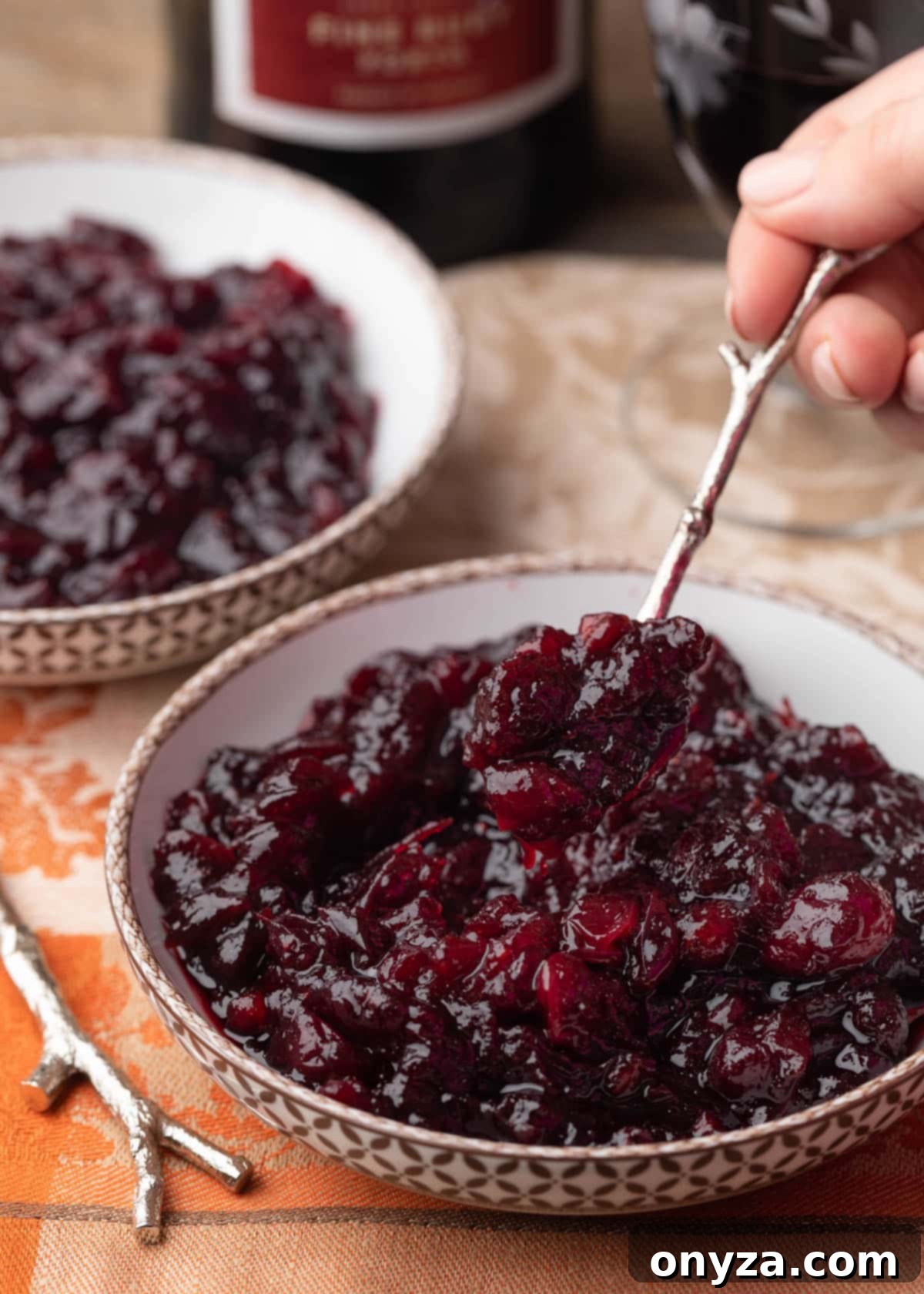 A spoonful of port cranberry sauce being held over a bowl of cranberry sauce on an orange damask napkin