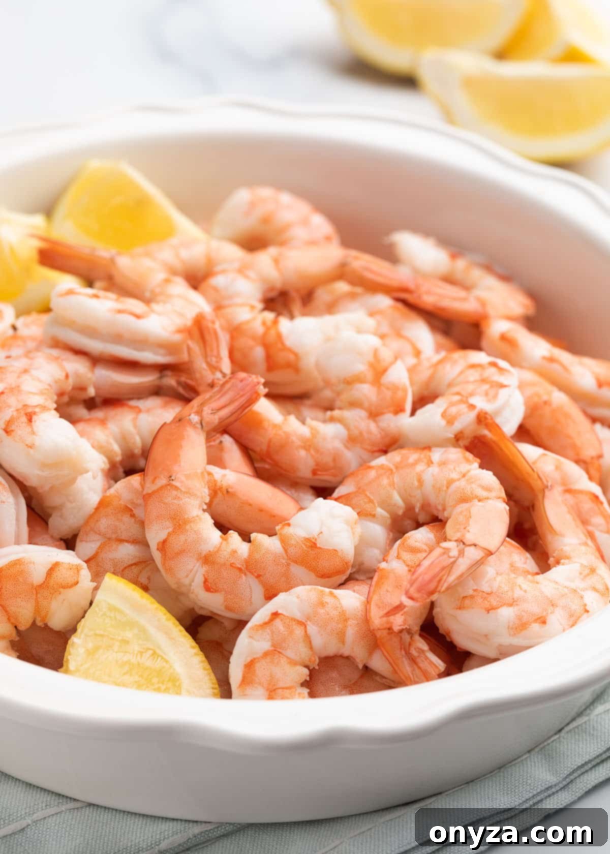 Beautifully peeled poached shrimp presented in a white pie plate, artfully arranged with fresh lemon wedges, ready for serving.