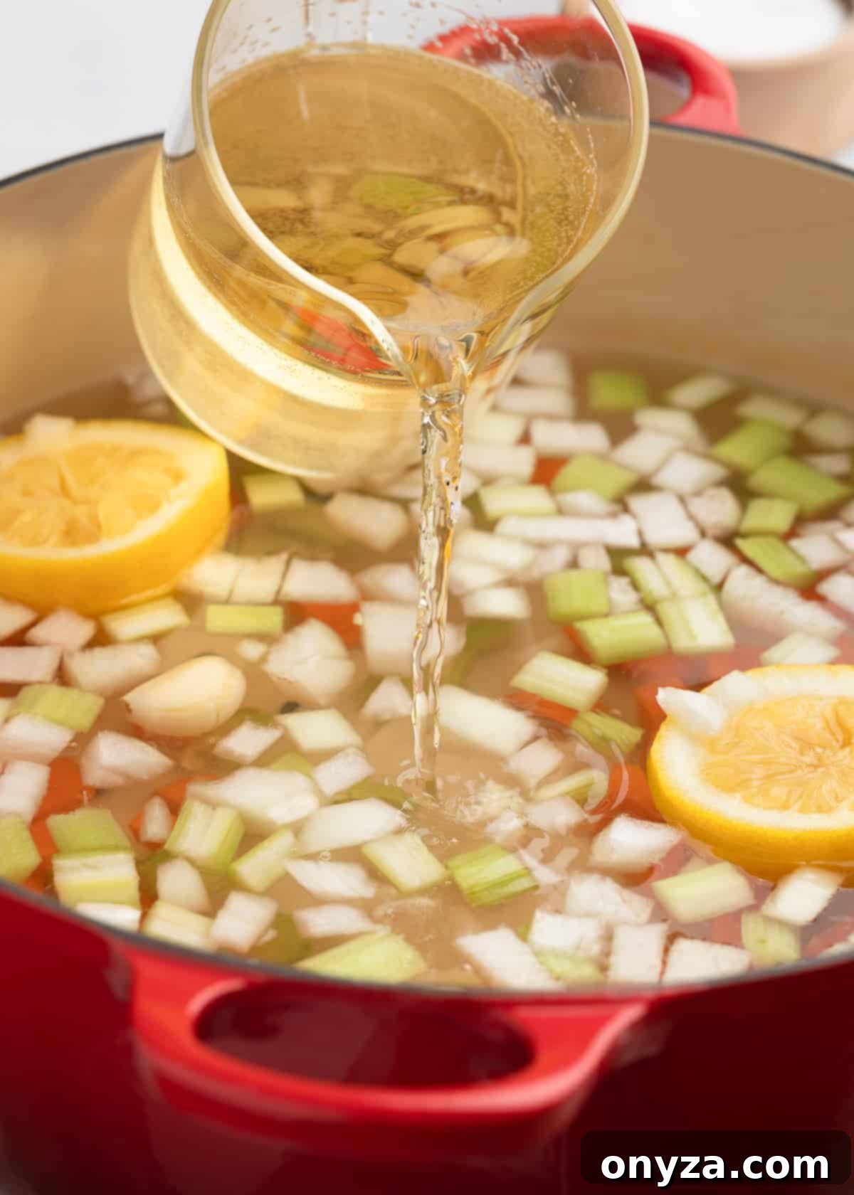 Pouring dry white wine from a glass measuring cup into a cast iron Dutch oven already containing water, diced vegetables, and lemon halves for the court bouillon.