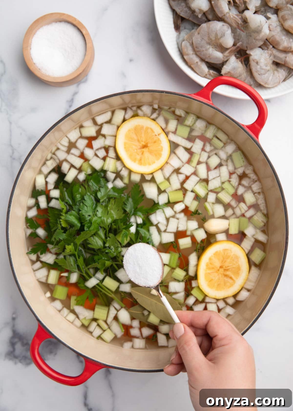 Overhead shot of kosher salt being measured with a tablespoon and added to the uncooked court bouillon mixture in a cast iron Dutch oven.