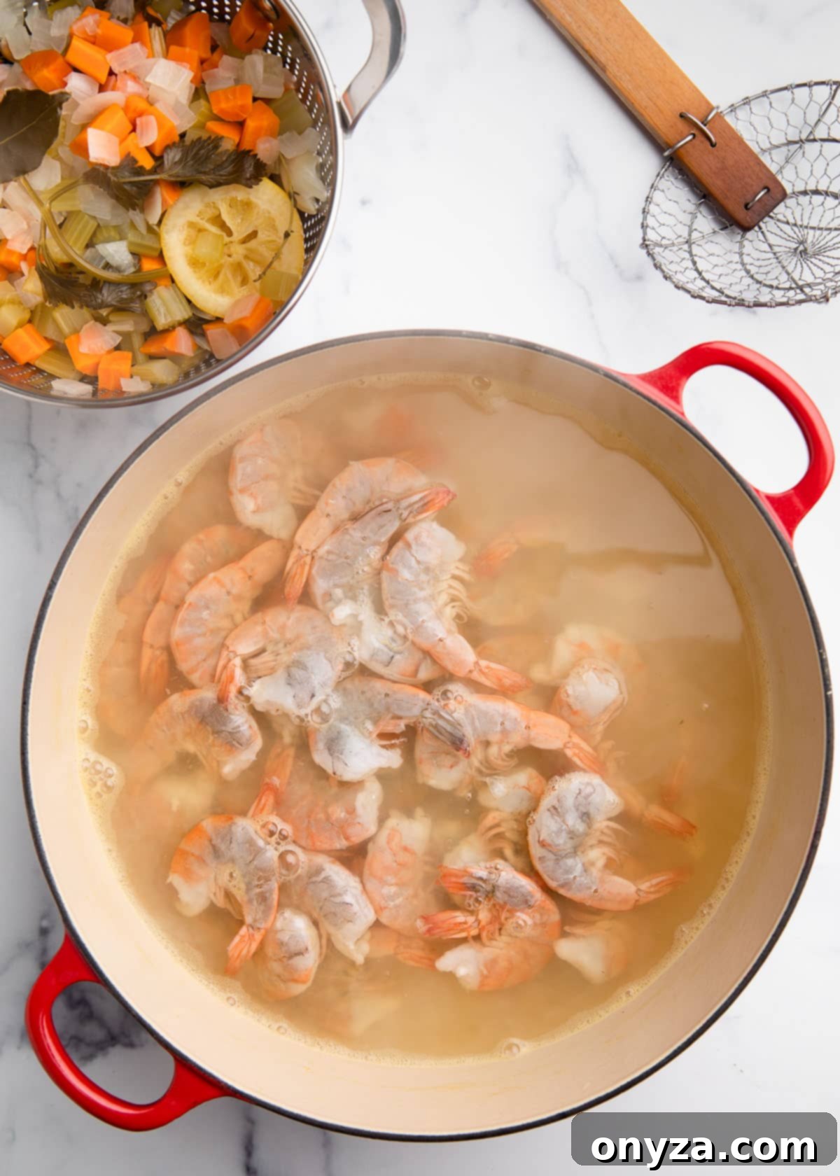 Overhead view of raw shrimp being carefully added to the freshly boiled poaching liquid within a Dutch oven, resting on a white marble board.