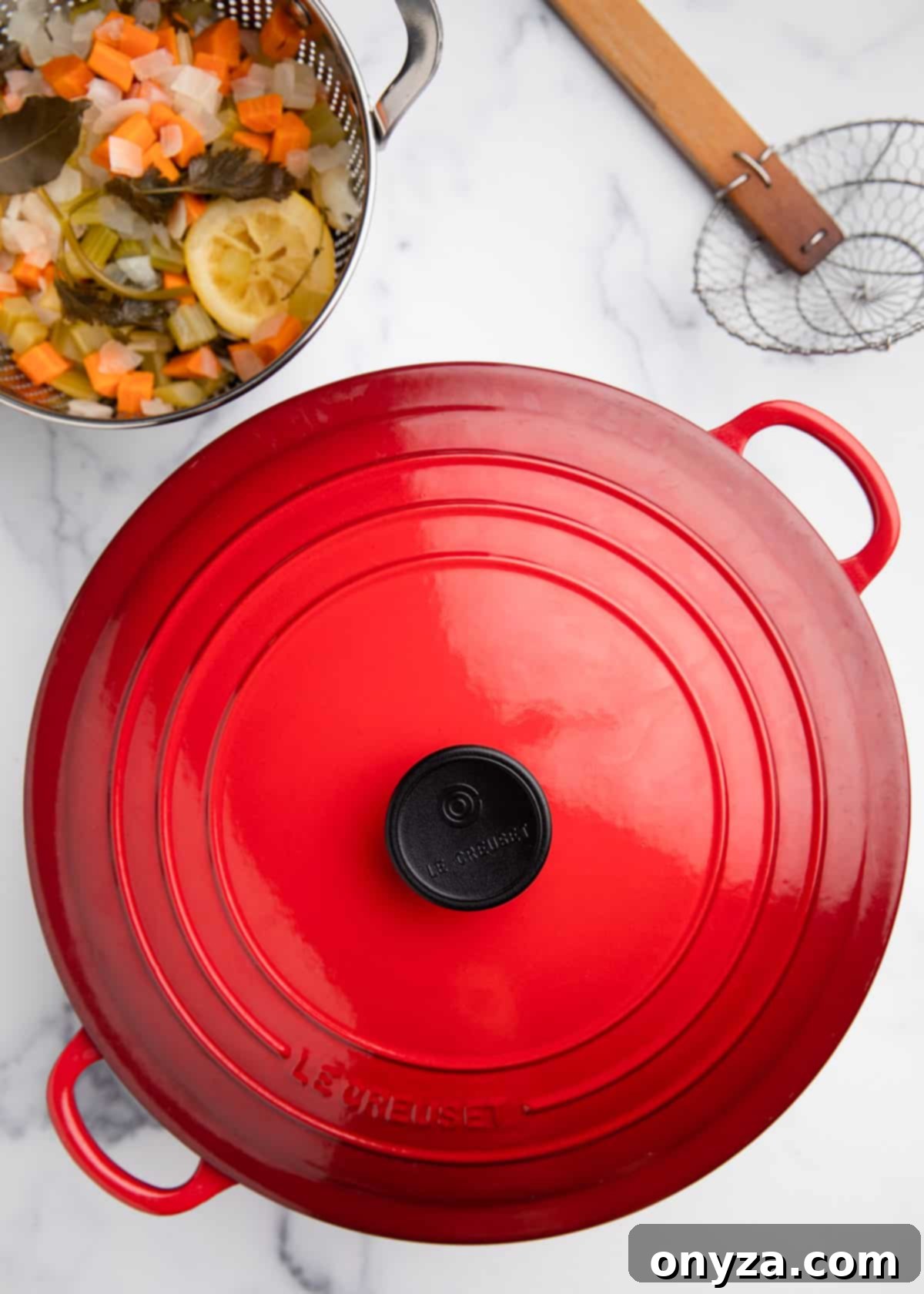 Overhead view of a covered red enameled Dutch oven resting on a white marble board, indicating the shrimp are cooking off direct heat.