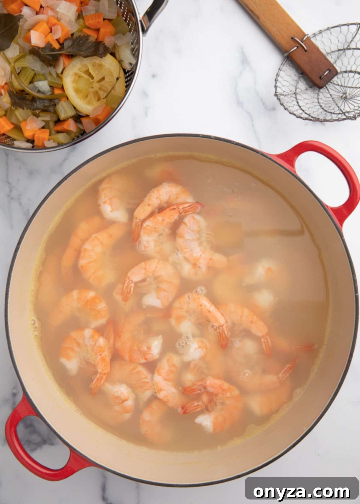 Overhead shot of freshly poached shrimp still in their cooking liquid within a Dutch oven, resting on a white marble board, uncovered after their cooking time.
