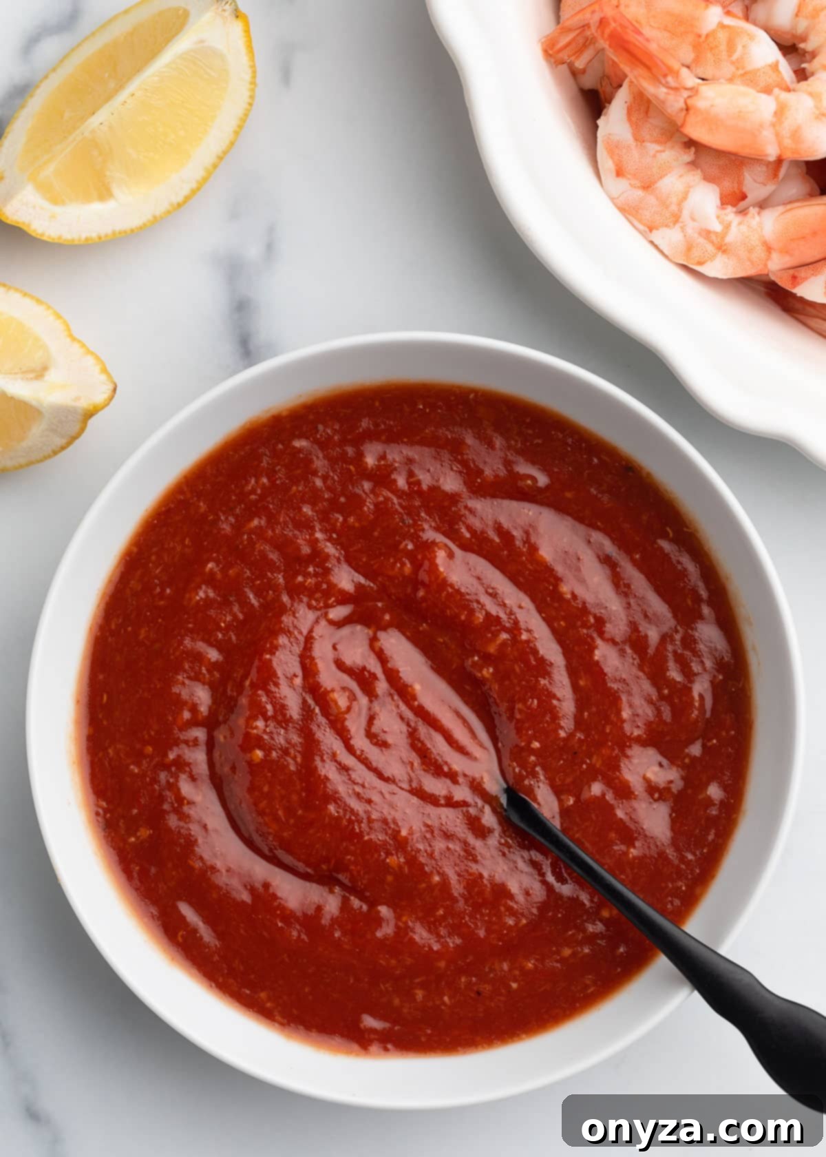 Zesty Homemade Cocktail Sauce 7 An overhead shot of perfectly mixed homemade cocktail sauce in a white bowl, with a black spoon resting inside, signifying it's ready for chilling.