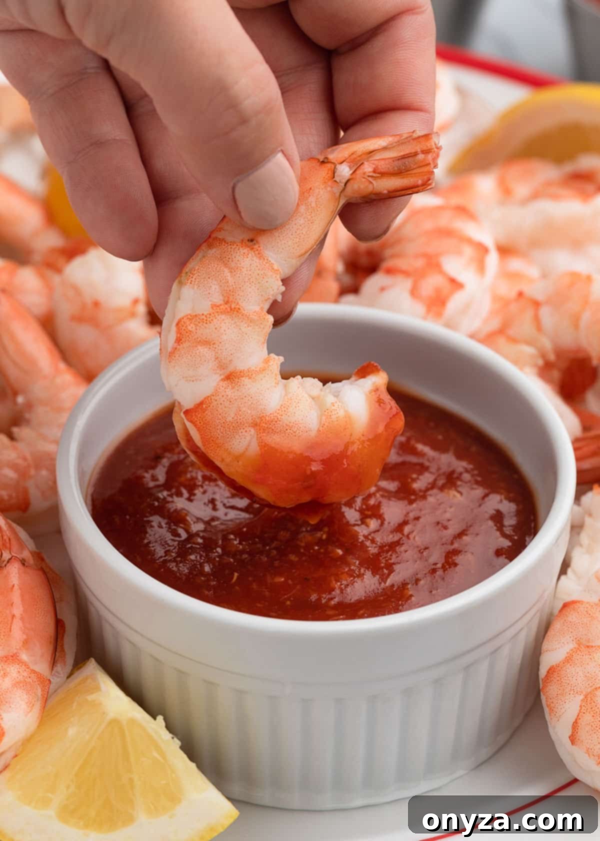 Zesty Homemade Cocktail Sauce 9 A close-up shot of a poached shrimp being dipped into a pristine white bowl of homemade cocktail sauce, highlighting the perfect pairing.