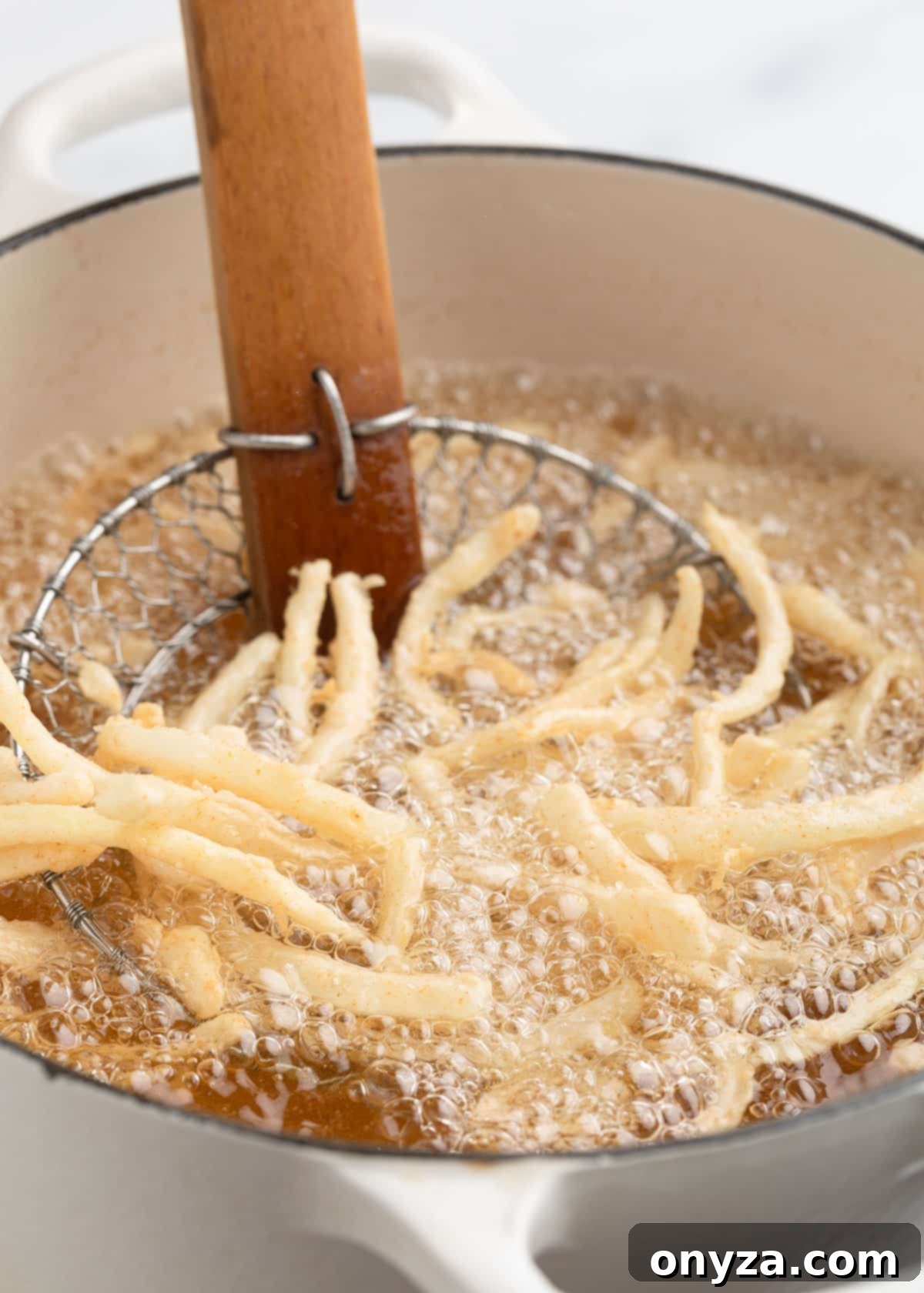 A dynamic shot of breaded onions actively frying in vigorously bubbling hot oil within a sturdy Dutch oven. They are just beginning to crisp and turn golden, ready to be transformed into perfect, delectable crispy strings.