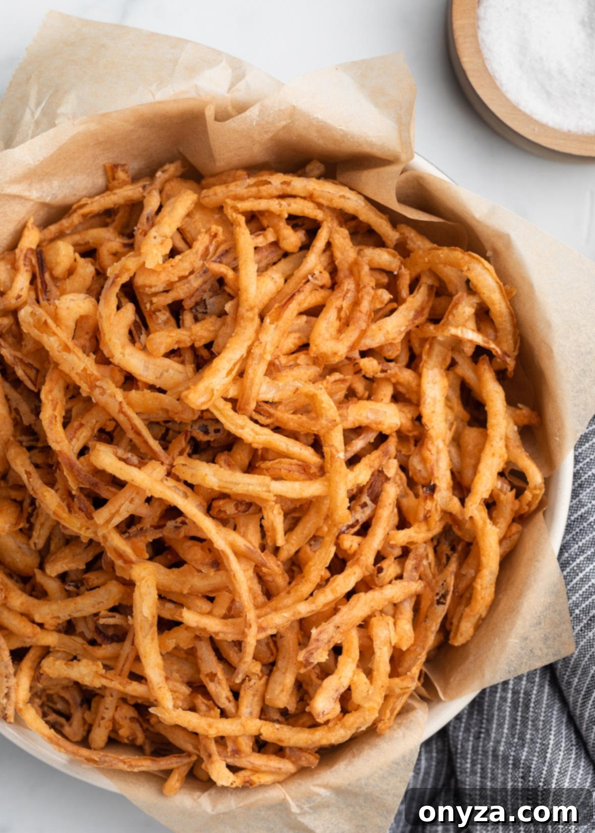 A beautifully arranged serving of homemade French fried onions in a bowl, showcasing their perfect golden color and enticing crisp texture. They are ready to be savored as a delicious topping or enjoyed as a delightful snack on their own.