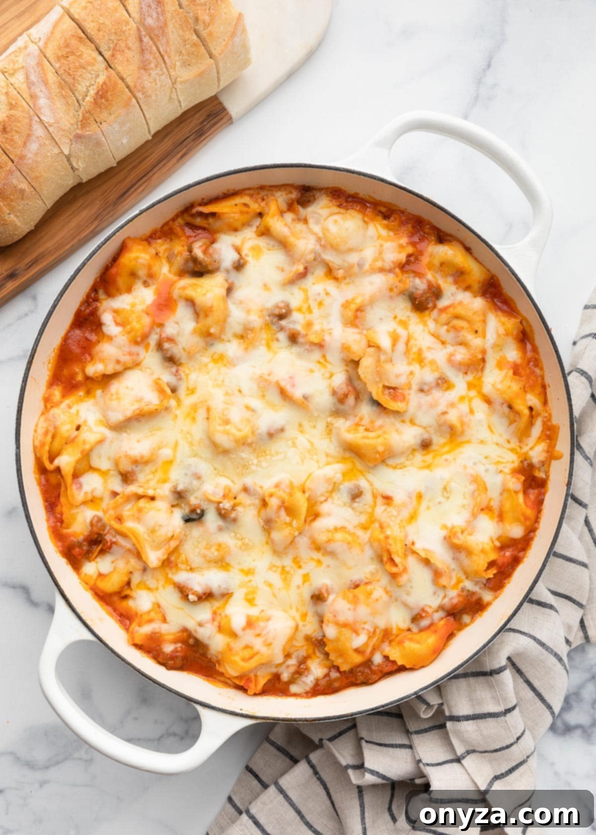 Overhead view of a baked tortellini sausage bake with perfectly melted mozzarella on top, served in a white enameled cast iron pot on a marble board.