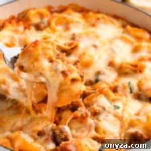 A close-up of a baked tortellini with sausage dish, showing the bubbly cheese and rich sauce.