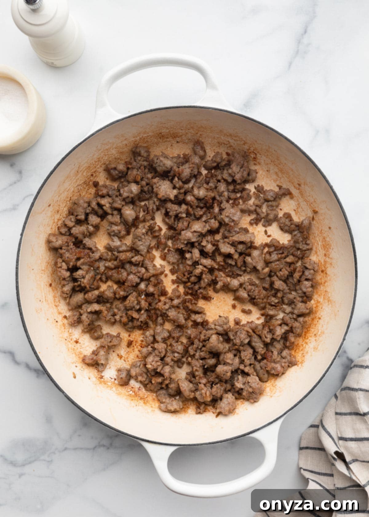 Beautifully browned, crumbled Italian sausage in a white enameled cast iron pot, ready for the next step.