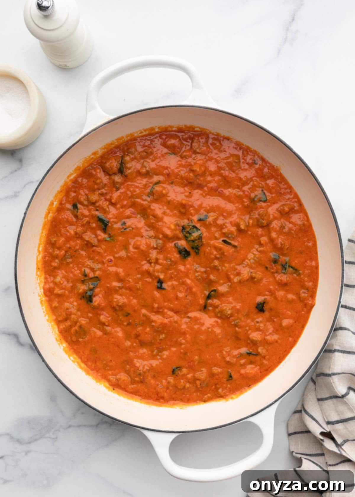 Creamy marinara sauce perfectly combined with crumbled sausage in a white enameled cast iron pot, showcasing its rich texture.