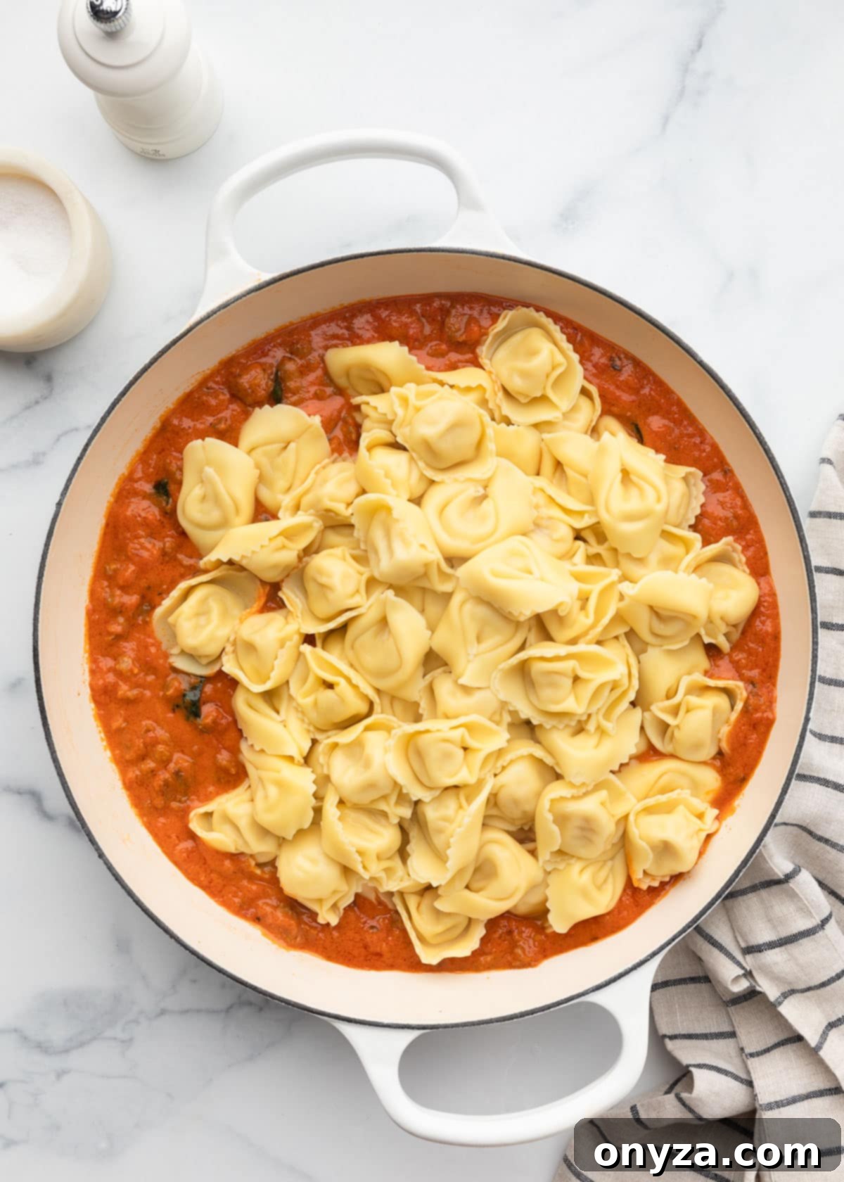 Cooked tortelloni resting on top of the rich marinara sauce in a white enameled cast iron pan, showing their perfect al dente state.