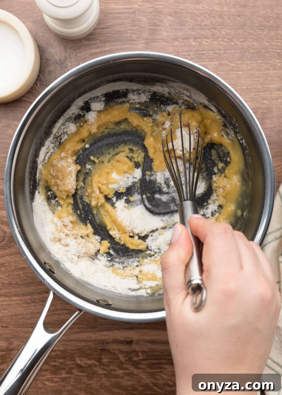 flour being whisked into melted butter in a pot on a wood board