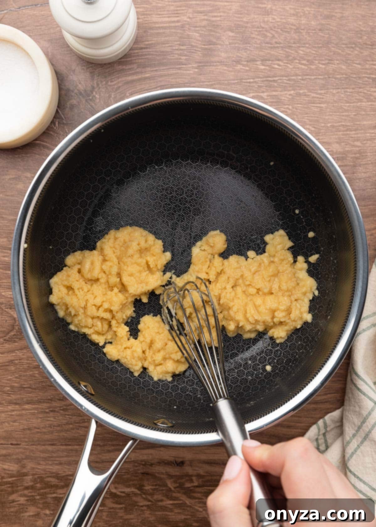 a thick roux being whisked in a pot on a wood board