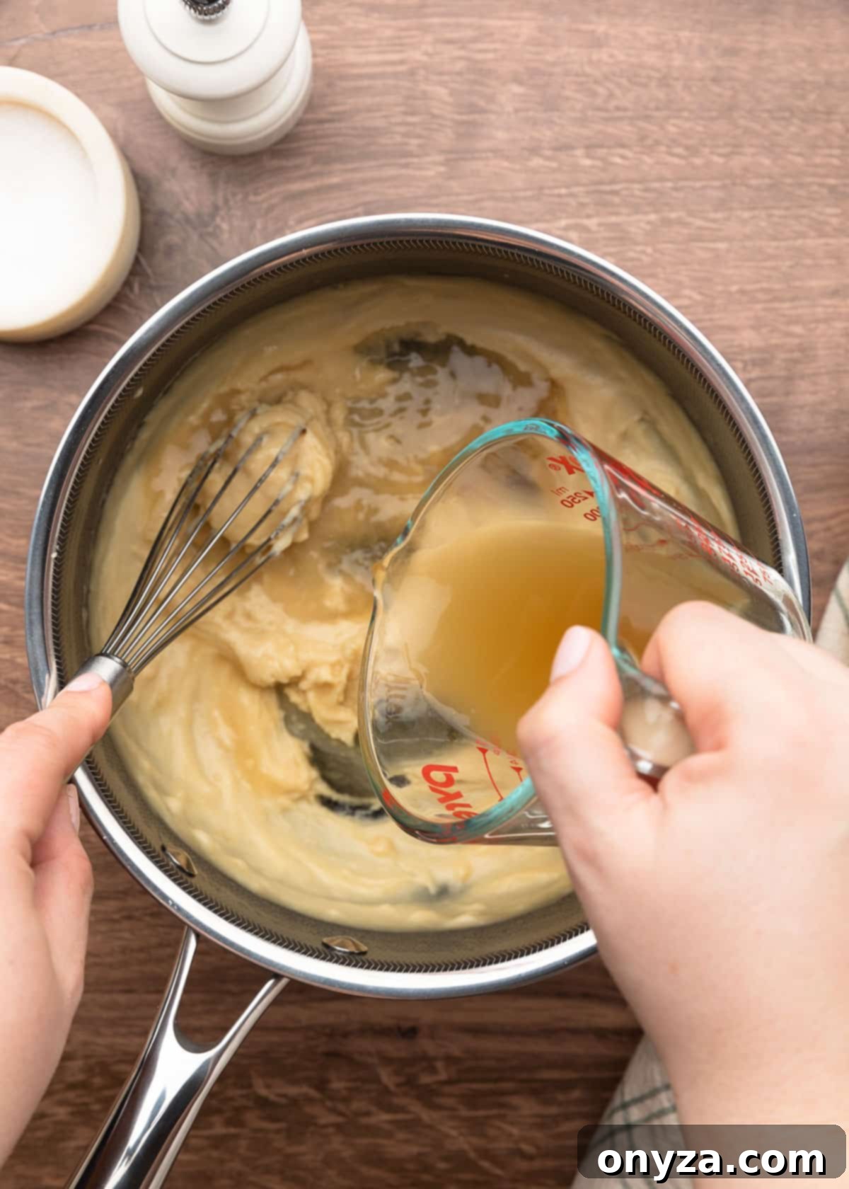chicken stock being poured from a measuring cup into a pot of cream of chicken soup while being whisked
