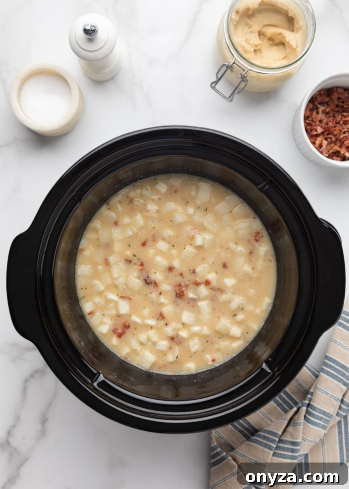 The crockpot, filled with uncooked hash brown potato soup ingredients, is covered and ready to begin the slow cooking process on a pristine marble board.