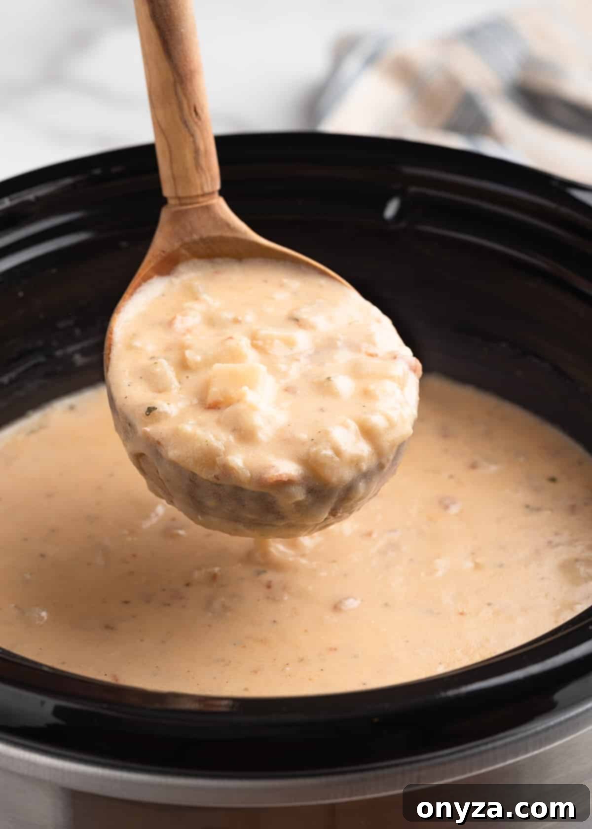 A ladle scooping a rich, creamy portion of hash brown potato soup from a slow cooker, showcasing its perfect texture and consistency approximately 15 minutes after cooking.