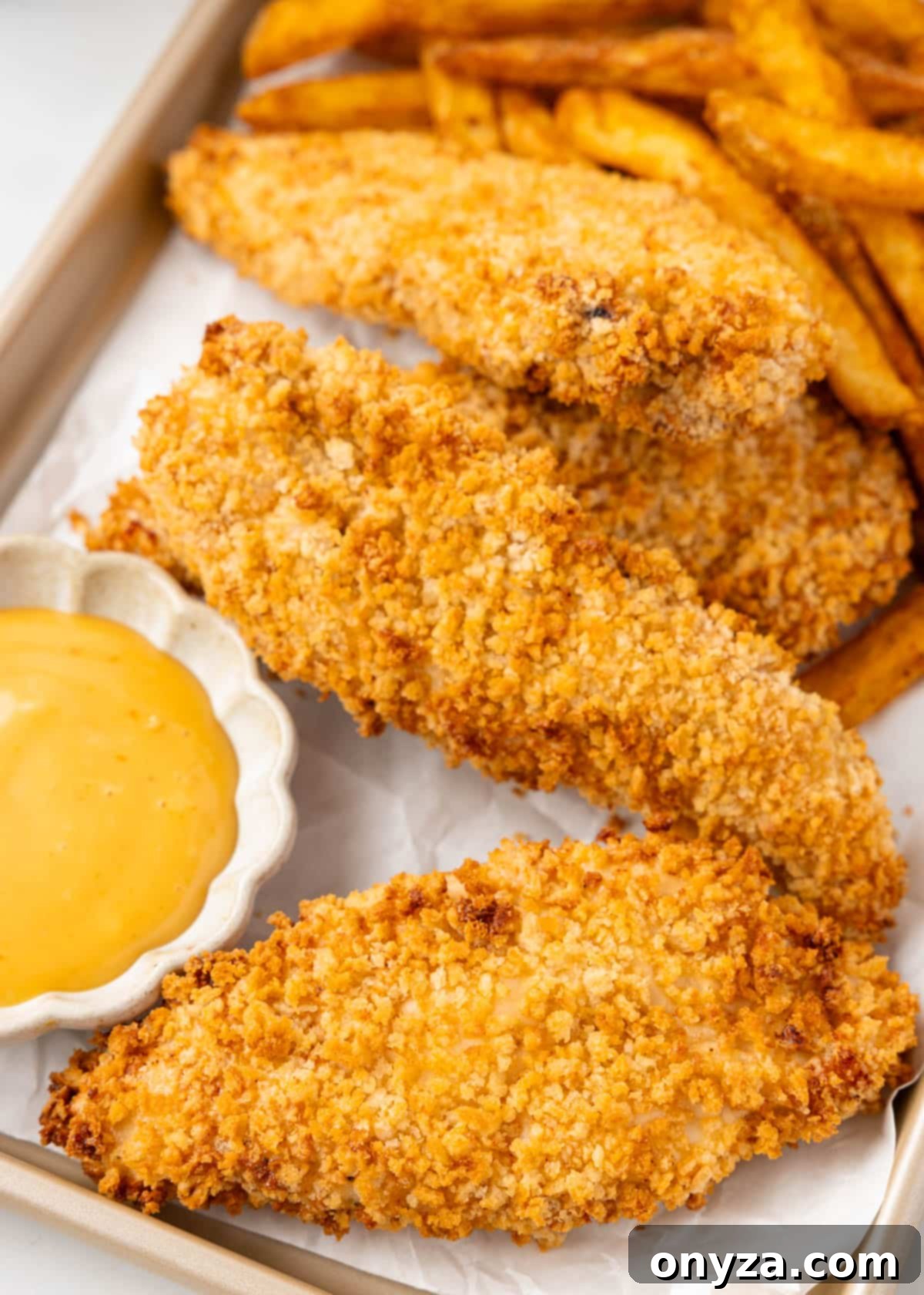 Crispy Air Fryer Chicken Tenders on a parchment-lined tray, served with honey mustard dipping sauce and golden french fries