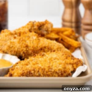 Perfectly golden-brown breaded chicken tenders on a parchment-lined baking sheet, showcasing their crispy texture