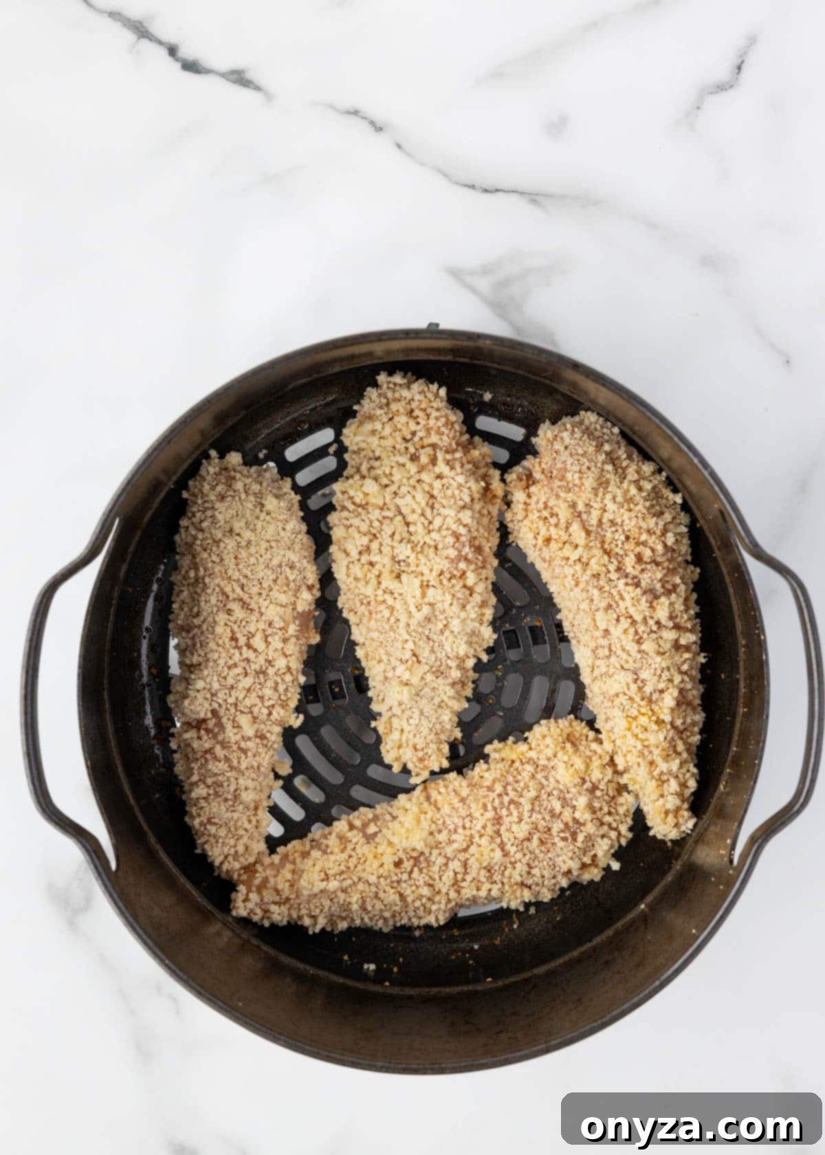 Uncooked breaded chicken tenders arranged in a single layer inside an air fryer basket, ready for cooking.