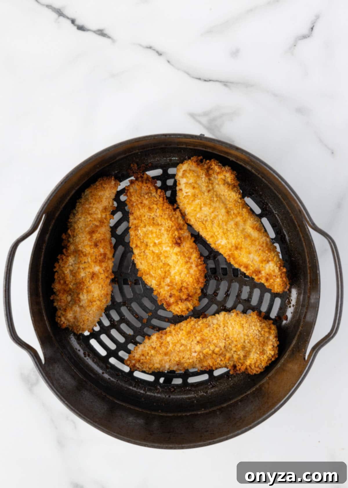 Cooked, golden brown, and crispy breaded chicken tenders perfectly air-fried in an air fryer basket.