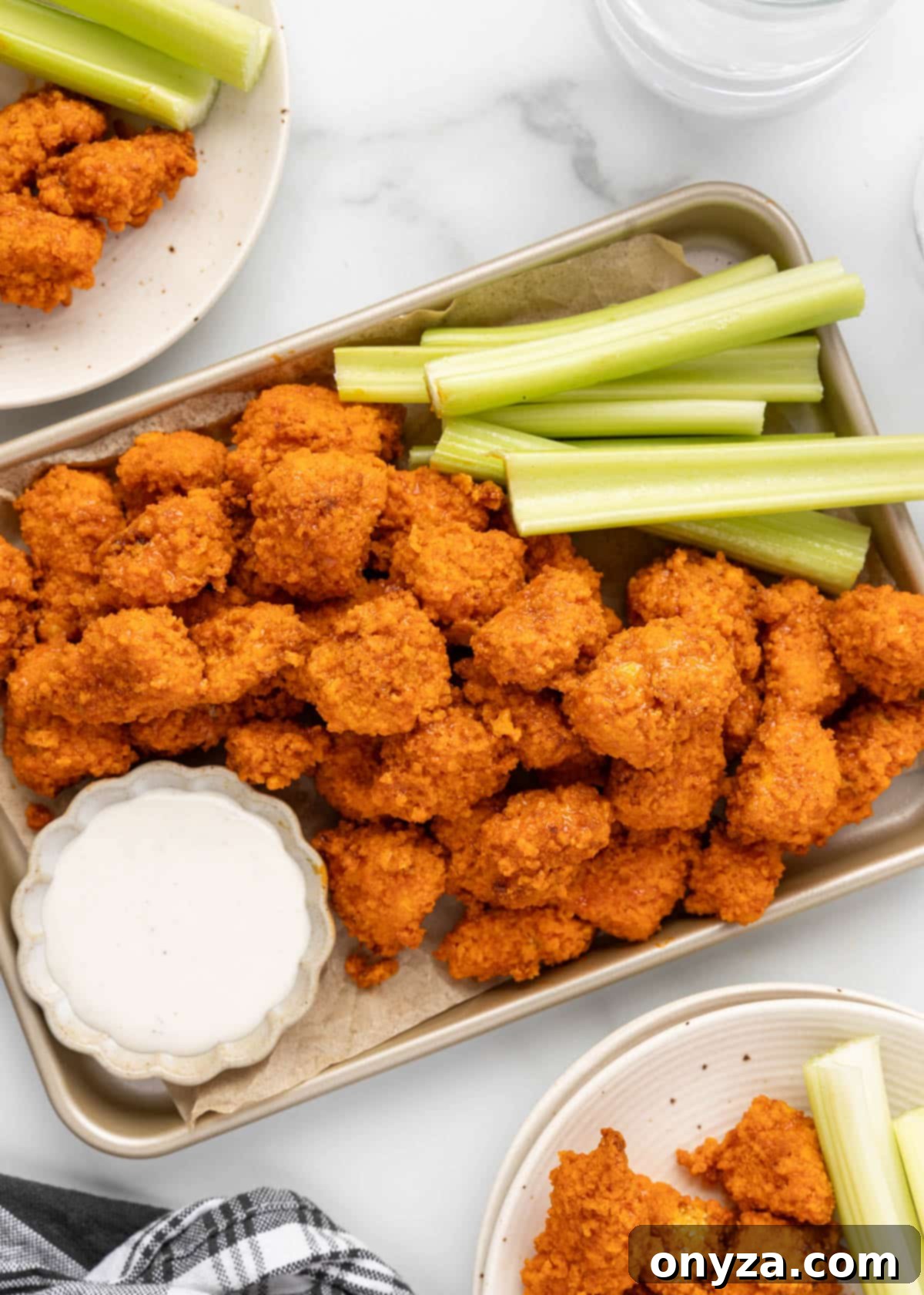 air fryer buffalo chicken bites on a parchment lined baking sheet with celery sticks and a bowl of ranch dressing