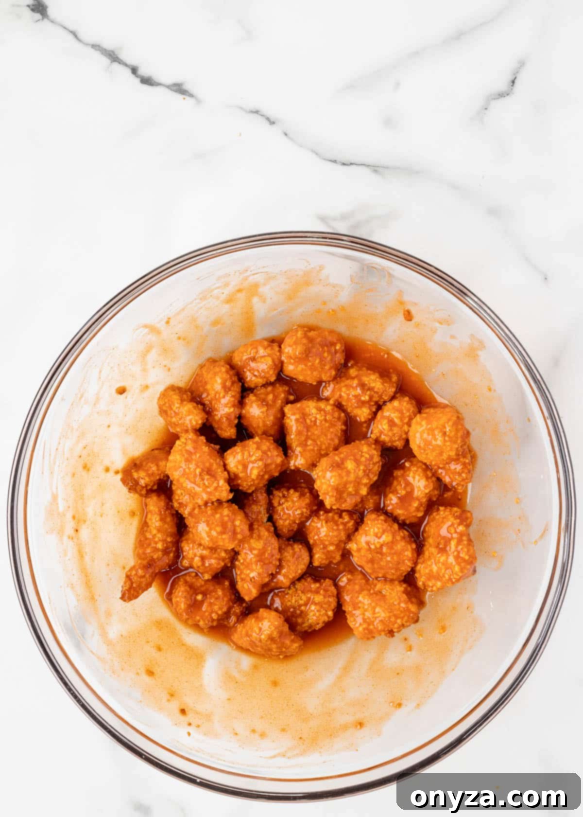 air fried buffalo chicken bites tossed in buffalo sauce in a glass bowl on a white marble board