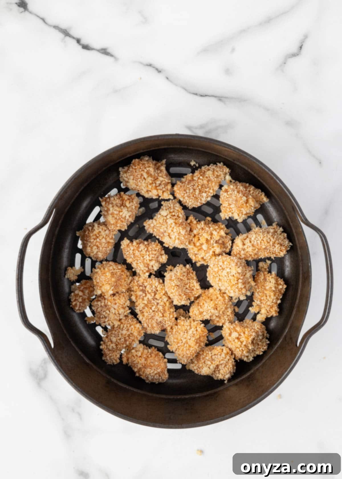 uncooked breaded buffalo chicken bites in an air fryer basket on a white marble board