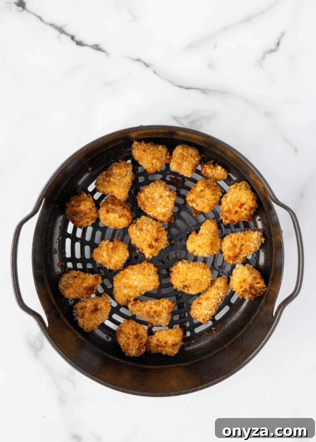 cooked breaded buffalo chicken bites in an air fryer basket on a white marble board